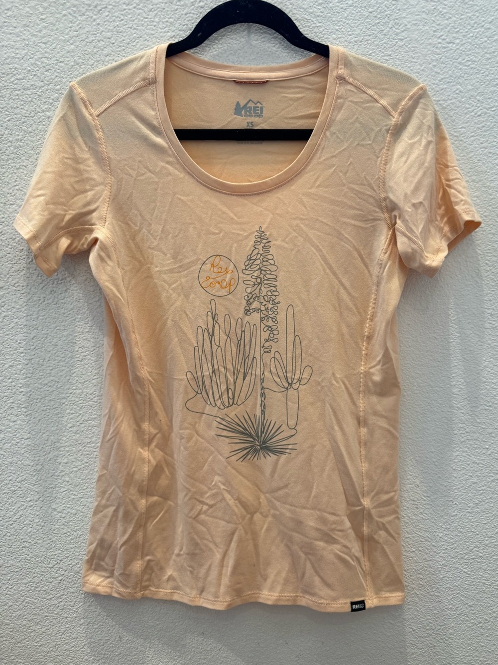 REI t-shirt features a graphic design of desert cacti and a sun